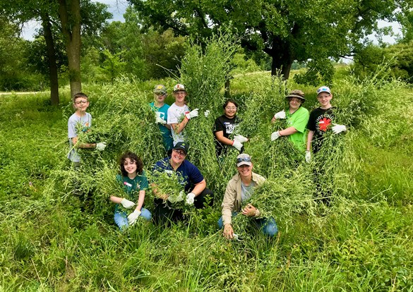 Two instructors with a group teens removing invasive species in the forest preserve.