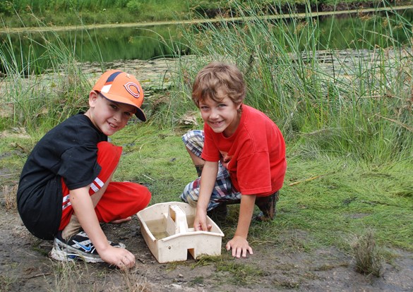 Two boys are playing in the dirt, laughing and having fun in a bright outdoor setting.