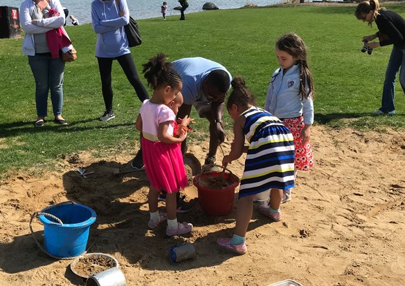 A group of children joyfully playing in the sand, building castles and digging with colorful buckets and shovels.