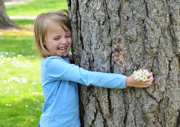 Young girl smiling as she wraps her arms around a tree and hugs it.
