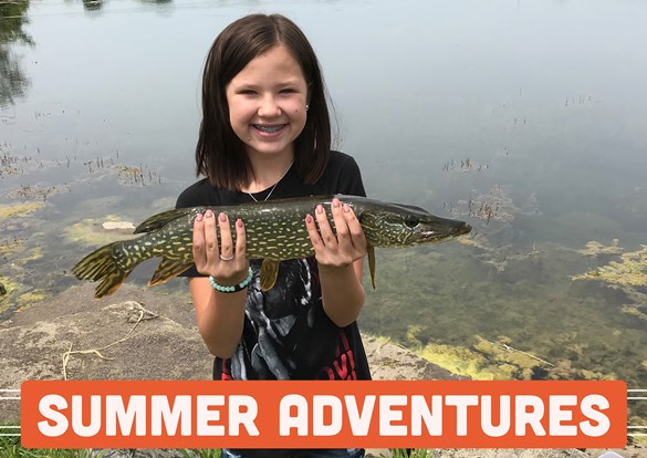 Yound girl standing in front of a pond holding a large Northern Pike fish