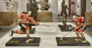 Two small metal sculptures of Chicago Black Hawk hockey players on wooden pedestals. 