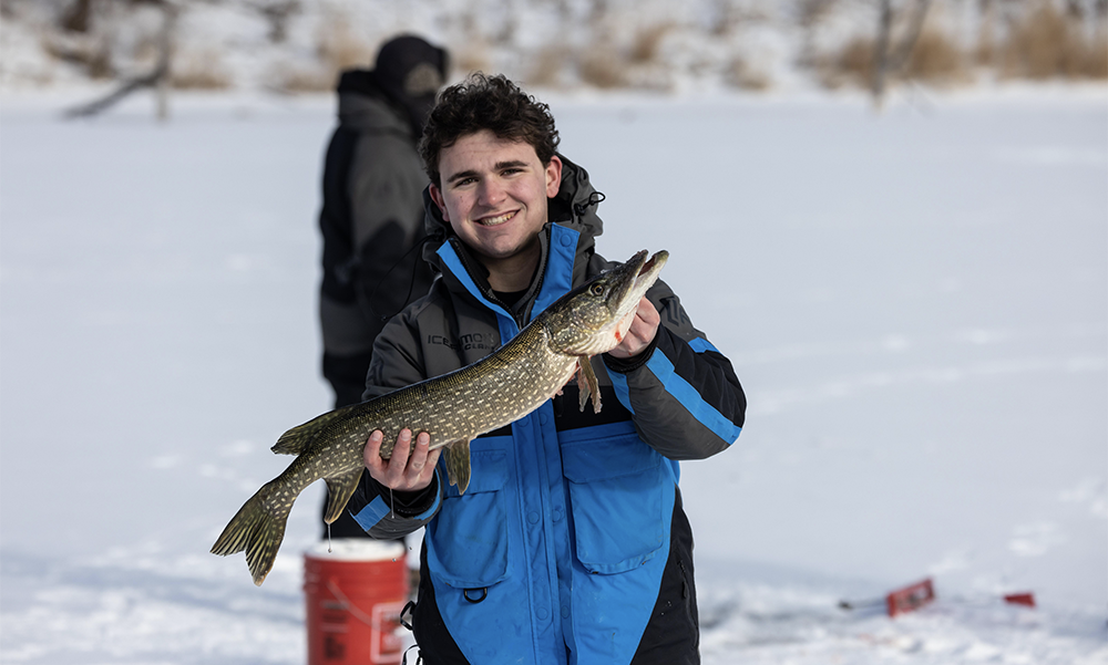 Young man with a big smile after catching a large northern pike while ice fishing.