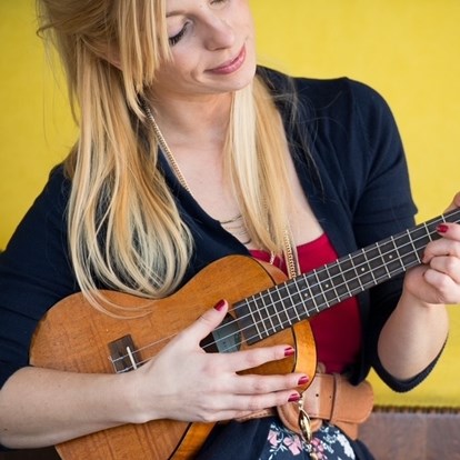 Woman in black sweater and flowered dress playing a Ukulele.