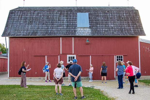 Group of people walking around an old red and white barn.
