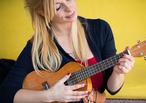 Woman in black sweater and flowered dress playing a Ukulele.