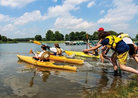 Group of young adults paddling kayaks across a lake.