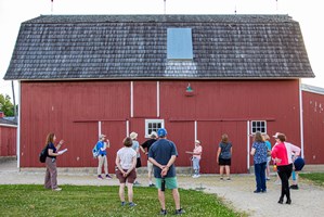 Group of people walking around an old red and white barn.