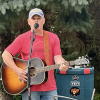Man in red t-shirt wearing a baseball cap playing a guitar.