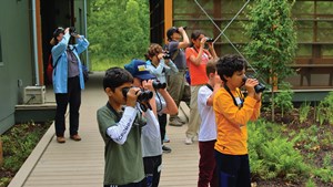 Group of young students with their instructors, all looking at birds with binoculars.