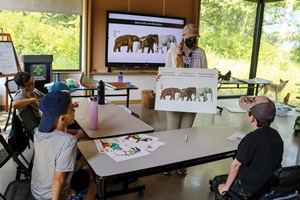 Instructor teaching a group of students about dinosaurs in a classroom.