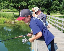 Instructor teaching young children how to fish on a pier.