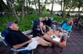 Friends gather in chairs near a a serene lake, sharing laughter and conversation under the clear blue sky.
