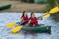 Two women in red life vests paddling a green kayak on the lake.