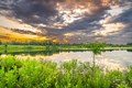 Gray and white clouds reflecting off the lake surruonded by green grass.