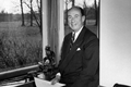 Adlai Stevenson sitting on his desk in front of a window.