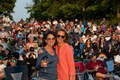 Two women smile and pose together at an outdoor concert, enjoying the lively atmosphere and music around them.