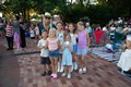 A group of smiling children stands with a woman, all posing happily for a photo together.