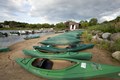Green kayaks lined up side by side on a sand beach.