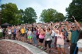 A lively crowd enjoying a band performance on stage, with people dancing and cheering in excitement.