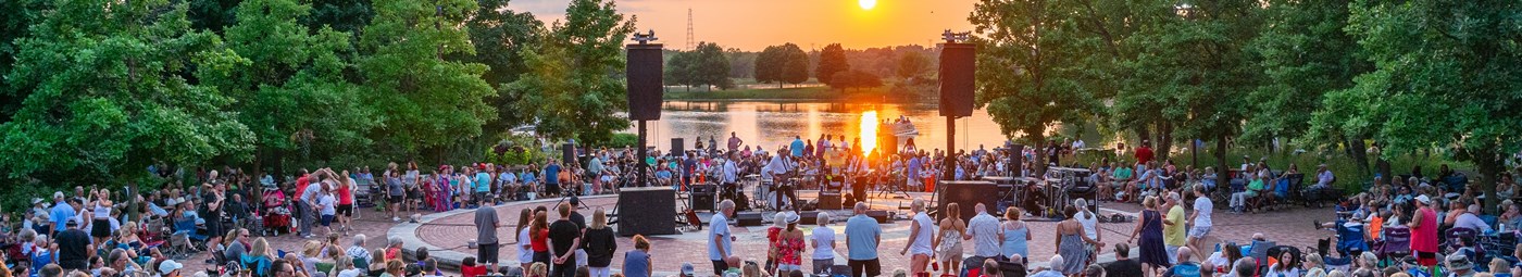 large crowd of people at outdoor concert by the lakeside.