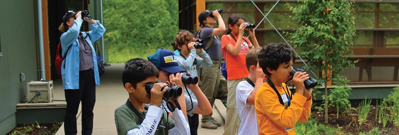 Group of young students with their instructors, all looking at birds with binoculars.