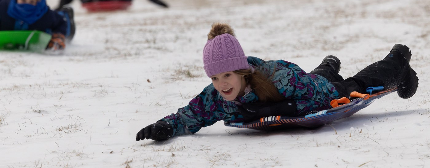Young girl sledding down a hill on her stomach