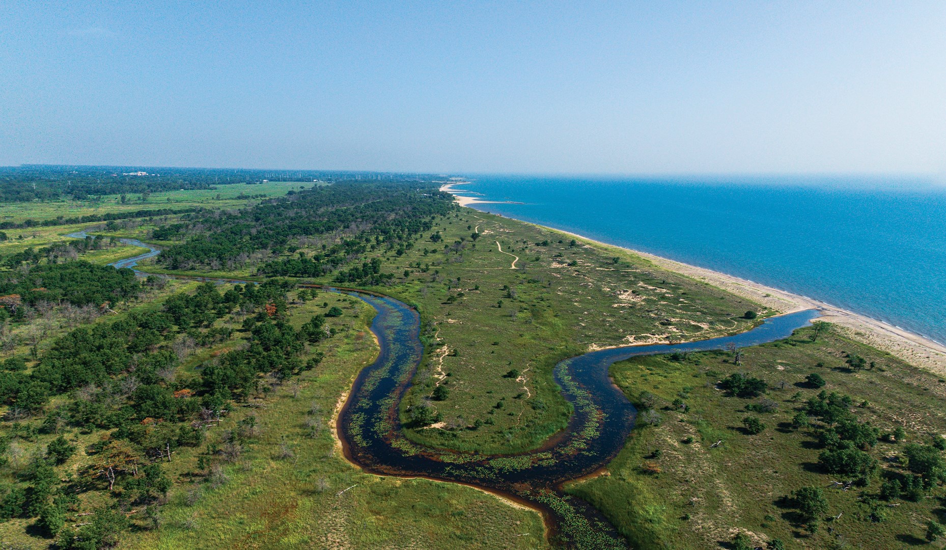Light blue skies, deep blue water, vibrant green shoreline.